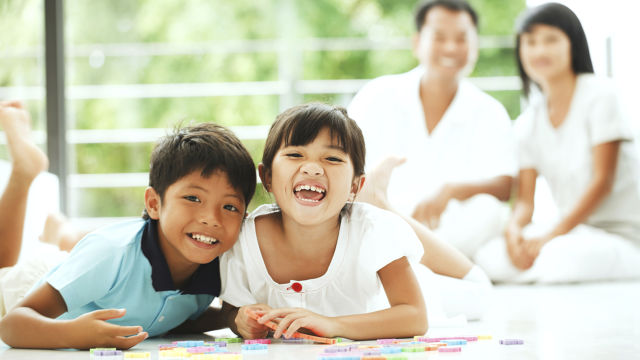 Des enfants regardant la caméra en souriant, avec leurs parents derrière
